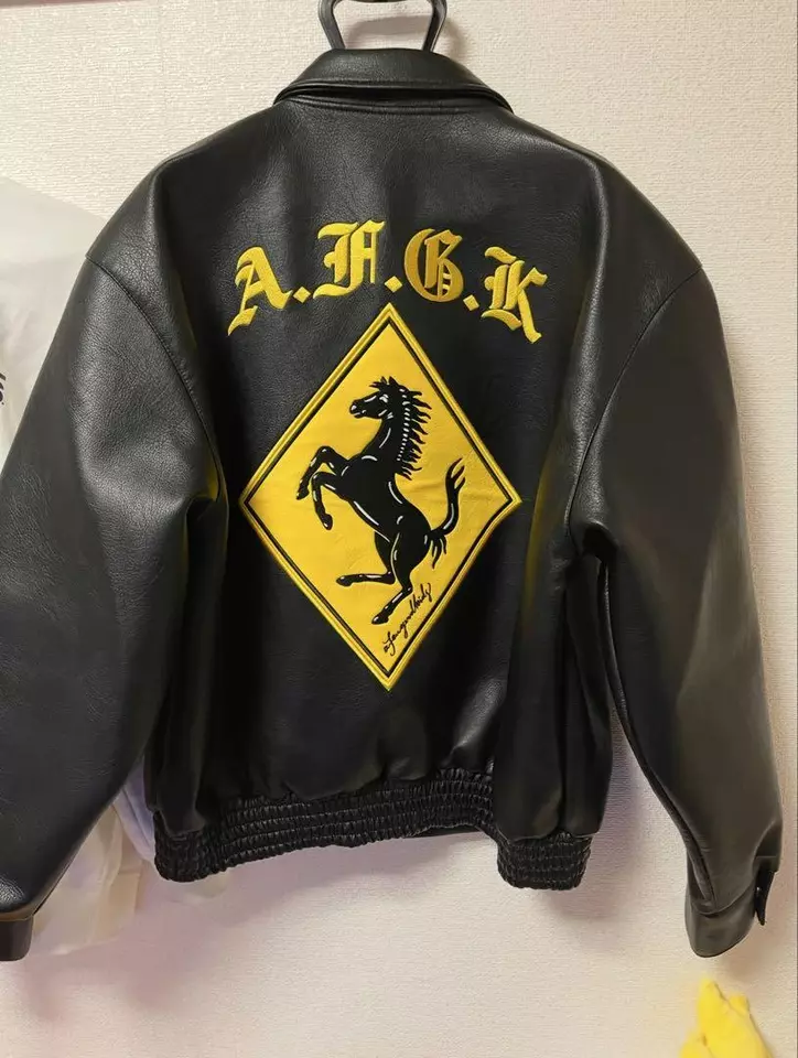 Back view of the black leather bomber jacket showing the yellow "A.F.G.K" text and diamond prancing horse emblem.
