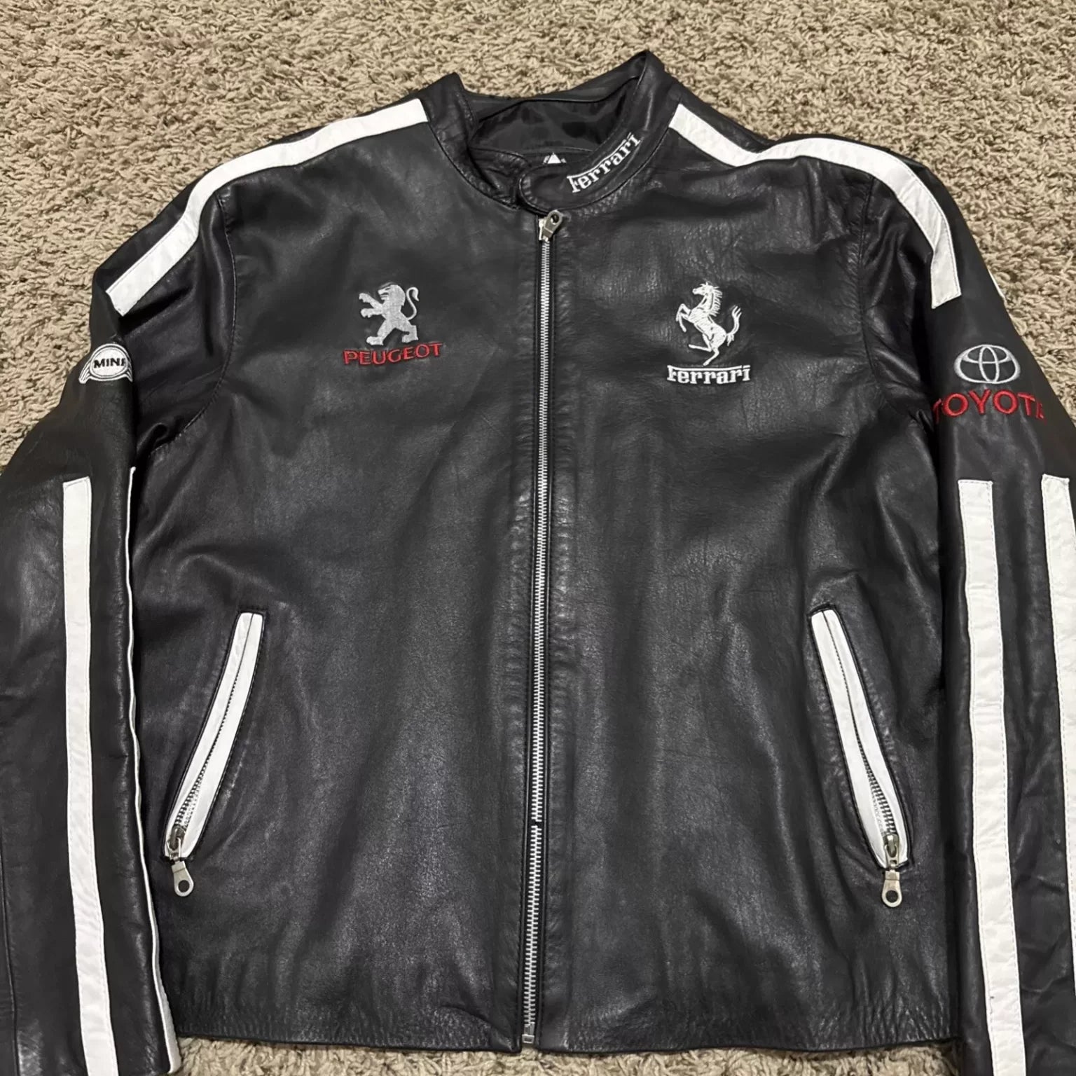Back view of the black leather jacket showing the large white Ferrari text, Corvette logo, and Audi logo.