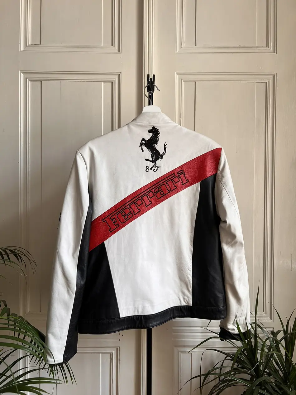 Back view of the white, black, and red Ferrari F1 racing jacket, prominently featuring a large black prancing horse logo and red diagonal Ferrari text.