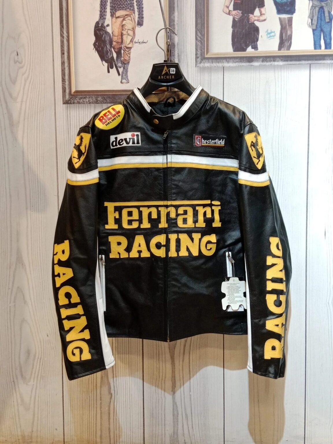 Full front view of a black leather Ferrari RACING jacket with bold yellow text, Bell Helmets, and Chesterfield sponsor patches.