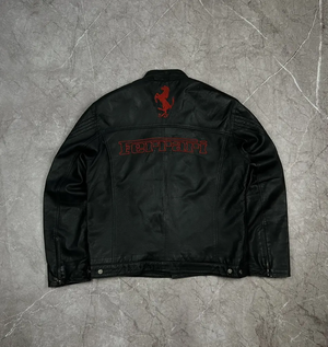 Back view of the black leather Ferrari jacket showing the red embroidered prancing horse logo and FERRARI text on a marble background.