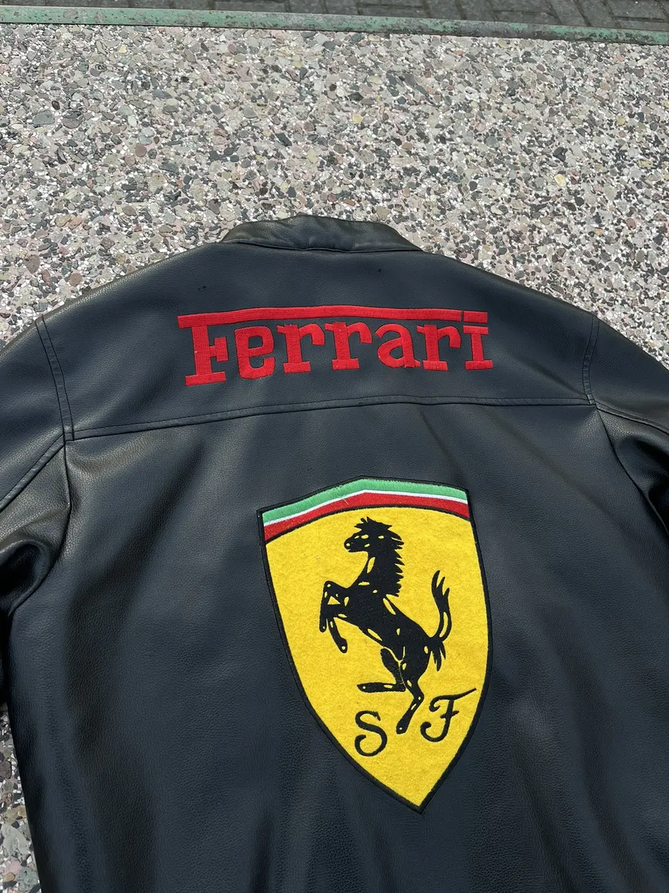 Back view of the black Ferrari F1 leather jacket showing the large red "Ferrari" text and the yellow Scuderia Ferrari shield.